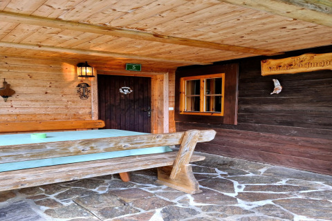 Außenbereich der Schneiderhütte in Österreich mit Holzgarnitur, Steinterrasse und rustikaler Fassade.