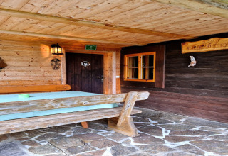 Außenbereich der Schneiderhütte in Österreich mit Holzgarnitur, Steinterrasse und rustikaler Fassade.