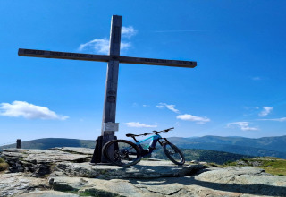 Fahrrad neben einem großen Holzkreuz auf dem Schneiderhütte in Österreich mit Bergpanorama.