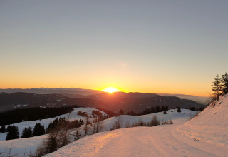 Sonnenuntergang über verschneiten Bergen bei der Schneiderhütte in Österreich mit Bäumen und Himmel.