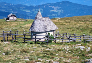 Piccola cappella con tetto di legno e recinto presso lo chalet Schneiderhütte in Austria, tra i monti.