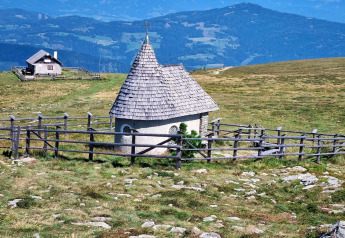 Et lille kapel med trætag og hegn ved Schneiderhütte i de østrigske bjerge, omgivet af grønne enge.