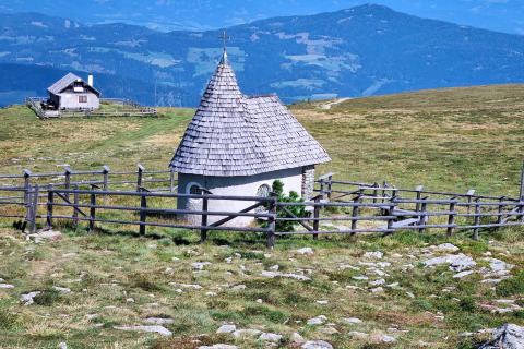 Kleines Kapelle mit Holzdach und Zaun nahe der Schneiderhütte in Österreichs Bergen, auf einer Almwiese.