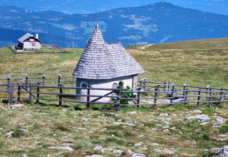 Kleines Kapelle mit Holzdach und Zaun nahe der Schneiderhütte in Österreichs Bergen, auf einer Almwiese.