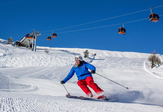 Ein Skifahrer fährt die Piste am Schneiderhütte-Chalet in Österreich hinunter bei strahlend blauem Himmel.