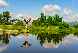 Una donna in equilibrio su una roccia vicino a un lago, riflessa nell’acqua, vicino allo chalet Schneiderhütte in Austria.