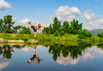 En kvinde balancerer på en sten ved en sø, reflekteret i vandet, nær Schneiderhütte i Østrig.