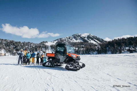 Gruppe Skifahrer und Schneemobil vor der Schneiderhütte im verschneiten Berggebiet in Österreich.