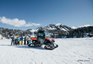 Group of skiers and a tracked vehicle in the snow at Alpenpark Turrach 21 in Austria, mountains behind.