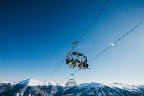 People riding a ski lift above snowy mountains at Alpenpark Turrach 21 chalet in Austria, under clear skies.
