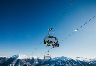 People riding a ski lift above snowy mountains at Alpenpark Turrach 21 chalet in Austria, under clear skies.