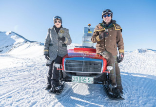 Two people in winter gear and goggles pose by a car-shaped snowmobile at Alpenpark Turrach 21, Austria.