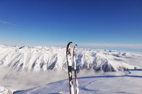 Two skis stand in snow overlooking snowy mountain peaks at Alpenpark Turrach 21, Austria, beneath a clear blue sky.