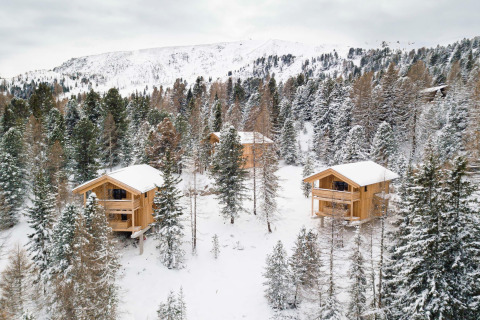 Sneeuwbedekte houten chalets in het bos bij Turracher Höhe, Oostenrijk, omringd door witte bergen.