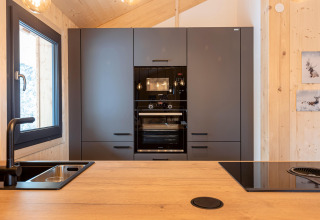 Modern kitchen in Nature Chalets Turracher Höhe 1, Austria, featuring black oven, window, and wood walls.