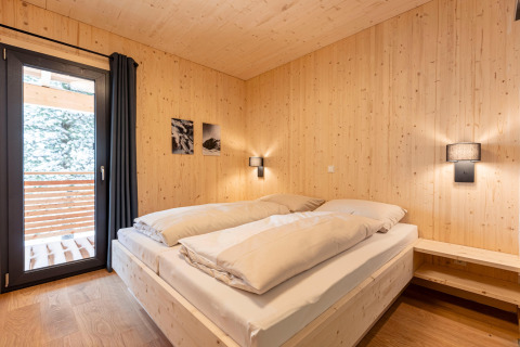 Bedroom in a tree house with wood-paneled walls and balcony at Nature chalets Turracher Höhe 1 in Austria.