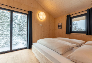 Bedroom in Nature chalets Turracher Höhe 1 tree house, Austria, with wood walls and snowy forest view.