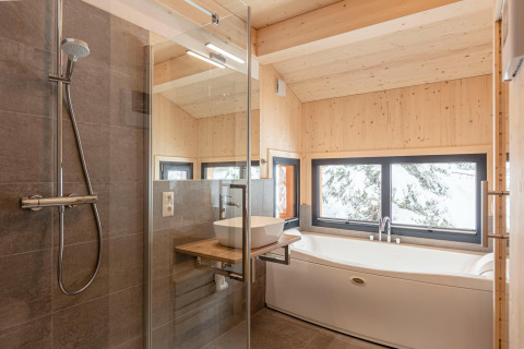Moderne badkamer in een boomhut in Oostenrijk met glazen douche, ligbad en uitzicht op de sneeuw.