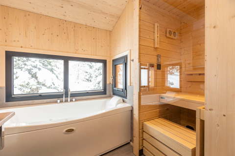 Modern bathroom in a tree house with a large bathtub, sauna, and window view of snowy trees in Austria.