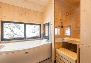 Modern badkamer in een boomhut met groot bad, sauna en ramen met uitzicht op besneeuwde bomen.