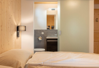 Bedroom in Nature Chalets Turracher Höhe 1 treehouse in Austria, showing bed, bathroom, and wood décor.