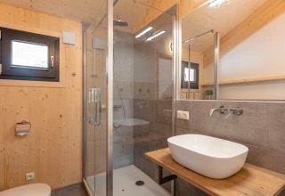 Moderne badkamer met houten wanden, glazen douche en waskom in Nature Chalets Turracher Höhe 1, Oostenrijk.