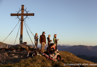 Wandelgroep geniet bij kruis op bergtop van zonsondergang op Turracher Höhe, Oostenrijk.