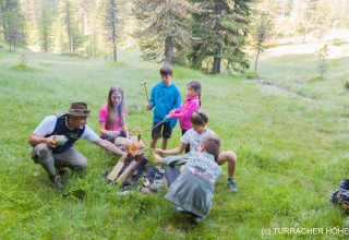 Group of children and an adult roasting sausages over a campfire at Nature chalets Turracher Höhe in Austria.