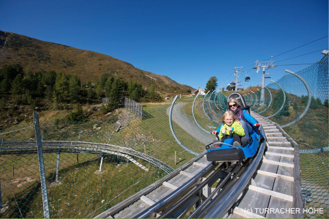 Een gezin rijdt in een alpine coaster bij Nature chalets Turracher Höhe, omgeven door bergen en natuur.