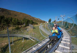 Een gezin rijdt in een alpine coaster bij Nature chalets Turracher Höhe, omgeven door bergen en natuur.