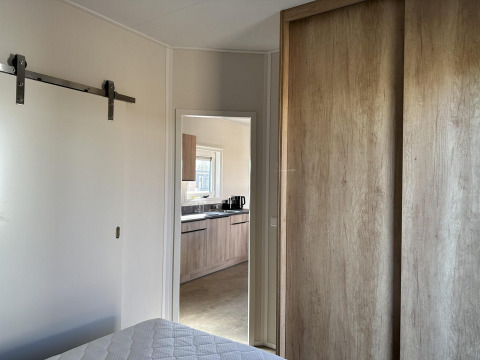 Slaapkamer met zicht op moderne keuken in Zonneweelde Lodge Deluxe op Camping Zonneweelde, Nederland.