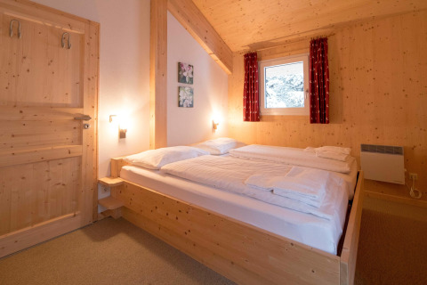 Cozy chalet bedroom at Alpenpark Turrach 21 in Austria with wooden walls, double bed, and window view.