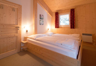 Cozy chalet bedroom at Alpenpark Turrach 21 in Austria with wooden walls, double bed, and window view.