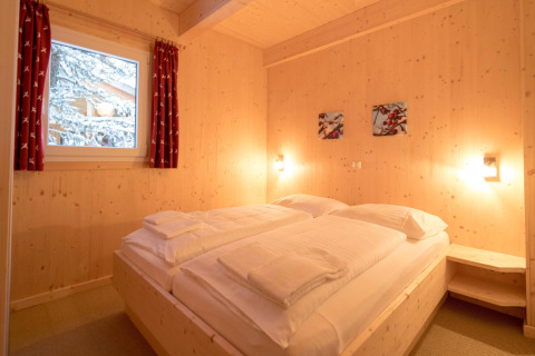 Cozy wooden bedroom with double bed, snowy window view at Alpenpark Turrach 21 chalet in Austria.