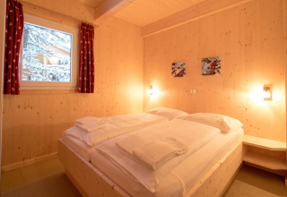 Cozy wooden bedroom with double bed, snowy window view at Alpenpark Turrach 21 chalet in Austria.