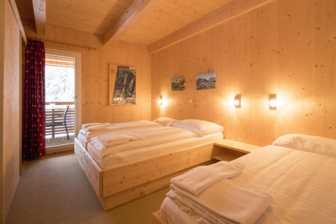 Wooden chalet bedroom at Alpenpark Turrach 21 in Austria, featuring twin beds and a balcony view.