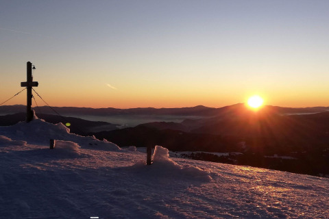 Sunrise over snowy mountains at the Alpenpark Turrach 21 chalet in Austria, with a cross and winter scene.