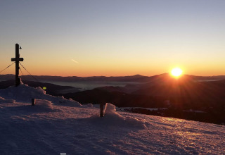 Sunrise over snowy mountains at the Alpenpark Turrach 21 chalet in Austria, with a cross and winter scene.