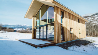 Modern wooden lodge Kreischberg Chalets 27 with large glass windows in a snowy mountain landscape.