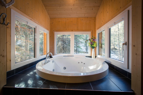 Modern round jacuzzi with black tiles, surrounded by windows overlooking forest at Alpenpark Turrach 21, Austria.