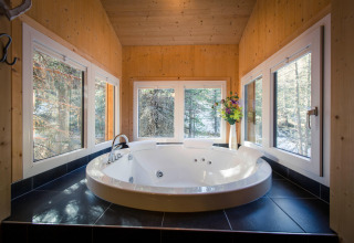 Modern round jacuzzi with black tiles, surrounded by windows overlooking forest at Alpenpark Turrach 21, Austria.