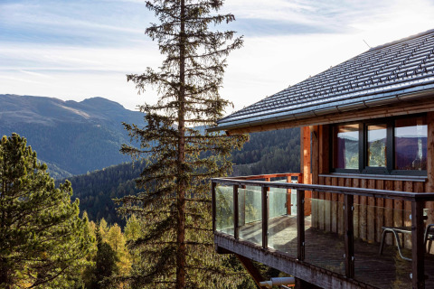 Wooden chalet with glass balcony at Alpenpark Turrach 21, Austria, overlooking scenic mountain views.