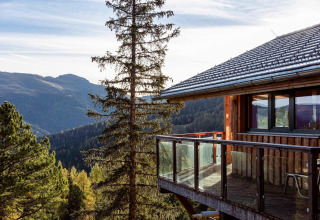 Wooden chalet with glass balcony at Alpenpark Turrach 21, Austria, overlooking scenic mountain views.