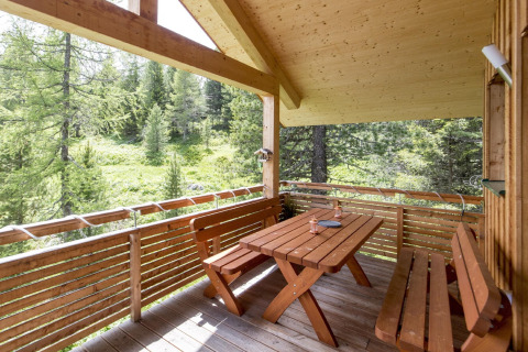 Wooden terrace with table and benches at Alpenpark Turrach 21 chalet, overlooking a lush forest in Austria.