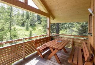 Wooden terrace with table and benches at Alpenpark Turrach 21 chalet, overlooking a lush forest in Austria.
