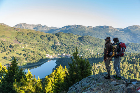 Two hikers admire the panoramic view from Alpenpark Turrach 21 chalet overlooking lake and mountains in Austria.