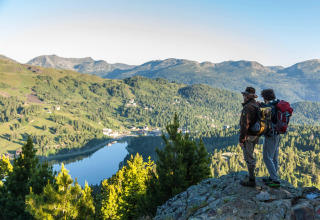 Two hikers admire the panoramic view from Alpenpark Turrach 21 chalet overlooking lake and mountains in Austria.