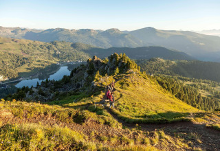 Hikers walking on a mountain ridge overlooking a lake and forests near Alpenpark Turrach 21 in Austria.