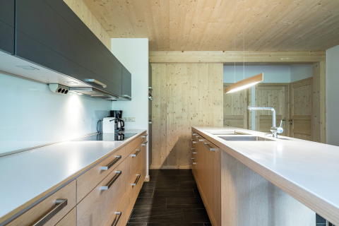 Moderne Küche im Kreischberg Chalets 21 in Österreich mit Holzverkleidung, weißen Arbeitsplatten und klaren Linien.