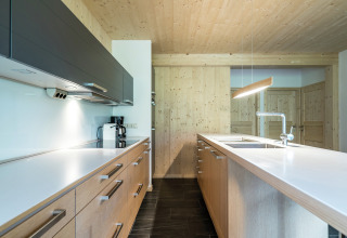 Moderne Küche im Kreischberg Chalets 21 in Österreich mit Holzverkleidung, weißen Arbeitsplatten und klaren Linien.